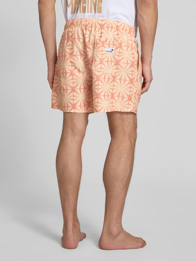 Männermodel trägt spodenki kąpielowe 'Badehose im Allover-Look mit elastischem Bund' von BOARDIES, wzór na całej powierzchni, krój regular fit, elastyczny pas, tunel, materiał w odcieniach beżu i pomarańczu, geometryczne kształty, gładka tekstura, Ganzkörperansicht Rückansicht.