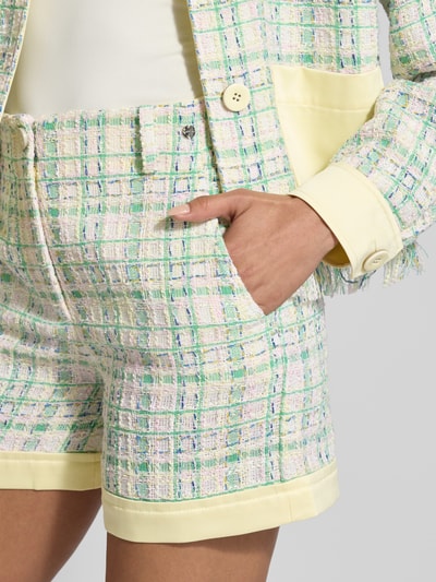 Frauenmodel trägt Wide Fit Shorts mit Label-Detail von Marc Cain, pastellig kariert im Allover-Look, High Waist, Detailaufnahme Hüfte.