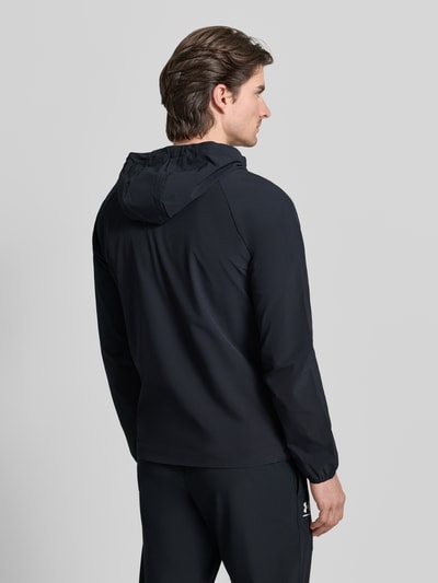 Mężczyzna prezentuje Jacke mit Kapuze von Under Armour, mieszanka materiałów z dodatkiem streczu, luźny krój, kaptur, tunel, zamek błyskawiczny, nadruk z logo, wpuszczane kieszenie, długość tyłu w rozmiarze M: 68 cm, długość rękawów w rozmiarze M: 66 cm, widok całej sylwetki z tyłu.