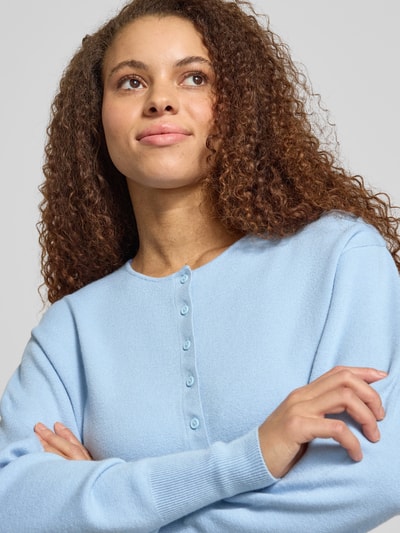 Kobiece modelka nosi Slim Fit Cardigan aus Viskose-Mix od Gina Tricot, krój regular fit, listwa guzikowa, okrągły dekolt, imitacja dzianiny, szerokie i elastyczne wykończenia; długość tyłu w rozmiarze S: 48 cm, długość rękawa: 59 cm, ujęcie: zbliżenie górnej części ciała.