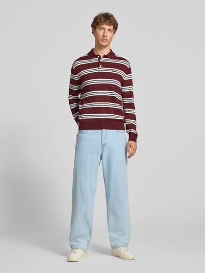 Männermodel trägt Strickpullover mit Polokragen von REVIEW in Bordeaux mit weißen Streifen, lockere Passform, Ganzkörperansicht von vorne.