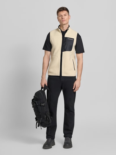 Männermodel trägt Weste mit Brusttasche Modell 'NatureRush' von PEAK PERFORMANCE in Beige und Schwarz, Fleece, Ganzkörperansicht von vorne.