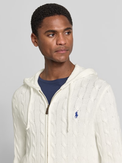 Męski model nosi Regular Fit kardigan rozpinany z czystej bawełny od Polo Ralph Lauren, kremowy kolor, tekstura warkoczowa, zbliżenie na górną część ciała.