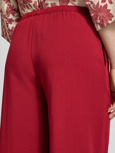 Kobiece modelka nosi Stoffhose aus Viskose-Mix mit Tunnelzug Modell 'Daria' od MSCH Copenhagen w czerwonym kolorze, tekstura lekko pomarszczona, detal tylnej partii talii, relaxed fit, szerokość w rozmiarze S: 39 cm, długość wewnętrzna nogawki: 78 cm, ujęcie z tyłu, zbliżenie na górną część spodni.