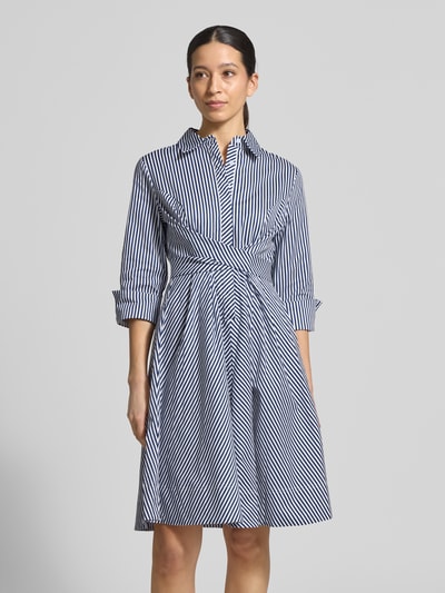 Modelka nosi Hemdblusenkleid mit Taillenband od Apricot, biało-granatowe paski, bawełna z domieszką elastanu, krój slim fit, midikleid, kołnierzyk kent, pasek w talii, rękaw 3/4, długość z tyłu w rozmiarze S: 110 cm, szerokość w rozmiarze S: 40 cm, długość rękawa w rozmiarze S: 50 cm, widok całej sylwetki z przodu.