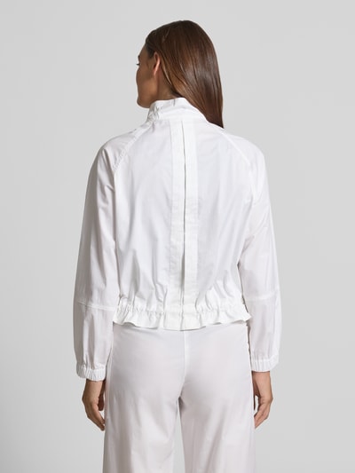Frauenmodel trägt Regular Fit Jacke mit Stehkragen von Marc Cain aus weißem Baumwoll-Mix mit Druckknopfverschluss, Bund mit Tunnelzug, elastische Ärmelabschlüsse, Rückenlänge 54 cm, Schulterbreite 40 cm, Brustweite 60 cm, Ärmellänge 72 cm, Ganzkörperansicht Rückansicht.