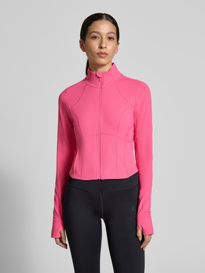 Frauenmodel trägt Slim Fit Jacke mit Stehkragen Modell 'Storm' von Fabletics in Pink, Crop Fit, Daumenschlaufen, Ganzkörperansicht von vorne.