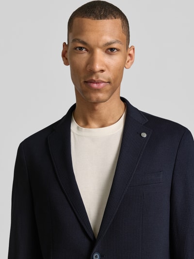 Męski model nosi Modern Fit Sakko mit Brustleistentasche od Pierre Cardin, ciemnogranatowy bawełniany miks, krój modern fit, detal z logo, kieszenie, zbliżenie na górną część ciała.