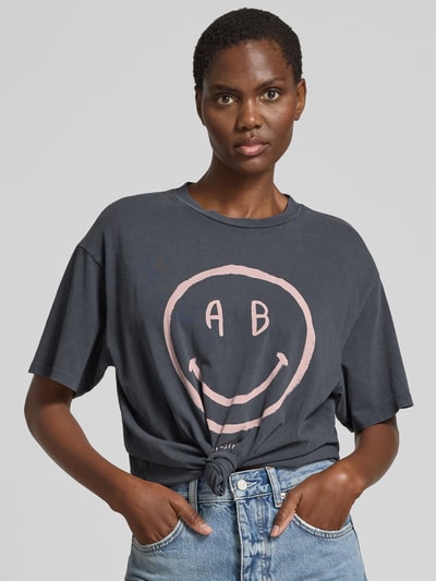 Frauenmodel trägt Relaxed Fit T-Shirt mit Logo-Print von Anine Bing aus reiner Baumwolle, dunkle Farbe, Rundhalsausschnitt, Kurzärmelig, Ganzkörperansicht von vorne. Rückenlänge in Größe S: 60 cm.
