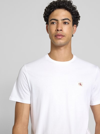 Männermodel trägt T-Shirt mit Label-Badge von Calvin Klein Jeans, biała bawełna, krój regular fit, okrągły dekolt, długość tyłu 70 cm, Nahaufnahme Oberkörper