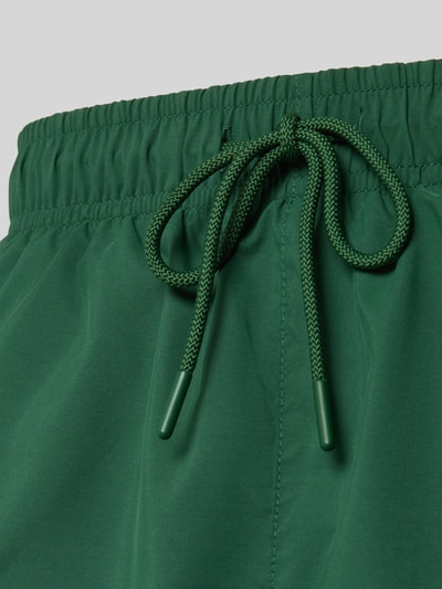 Produktfoto, Badeshorts mit Logo-Stitching von Lacoste, Optik: Unifarben, Tunnelzug, Bundabschluss: Elastisch, Funktion: Schnelltrocknend, seitliche Eingrifftaschen, grüne Oberfläche, glatte Textur.