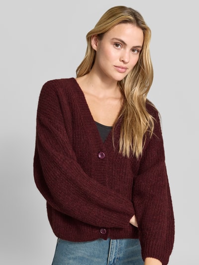 Frauenmodel trägt Oversized Cardigan mit Alpaka-Anteil Modell 'East' von American Vintage in bordeaux, Strick-Optik, Nahaufnahme Oberkörper.