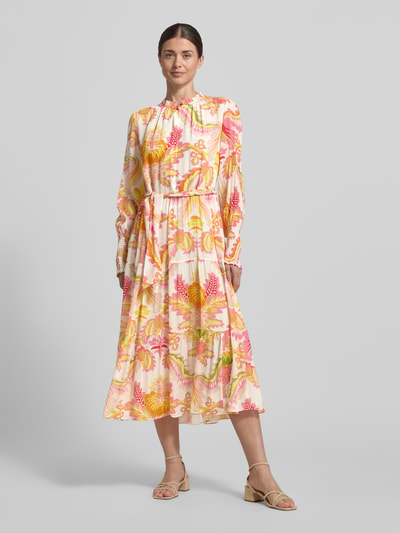 Frauenmodel trägt Regular Fit Midikleid aus reiner Viskose mit Stehkragen von HERZENS, floraler Allover-Print, Strukturmuster, Langärmelig, taillierte Passform mit abnehmbarem Stoffband, cremefarbene Basis mit gelben und pinken Details, Ganzkörperansicht von vorne.