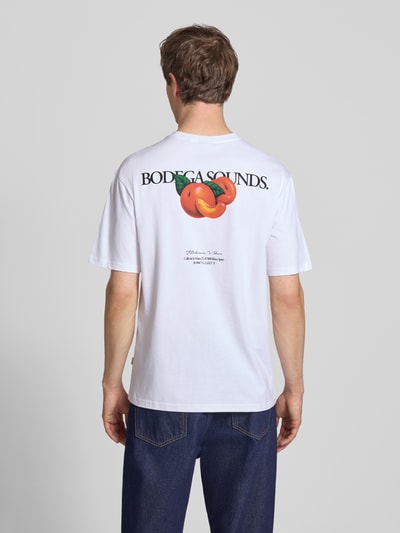 Männermodel trägt Relaxed Fit T-Shirt aus reiner Baumwolle Modell 'TASTY' von Only & Sons, weiß, Rückseite mit Schriftzug-Print und Rücken-Print, Rundhals, kurzarm, Ganzkörperansicht Rückansicht.