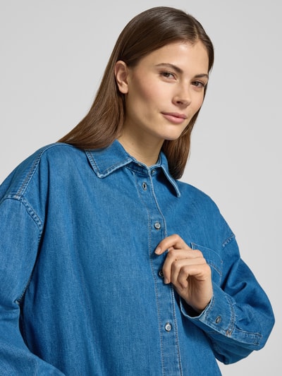 Frauenmodel trägt Relaxed Fit Jeansbluse aus reiner Baumwolle Modell 'FOGGIA' von Weekend Max Mara in Denim-Optik mit Kontrastnähten, einreihiger Knopfleiste, Hemdkragen und Brusttasche, Nahaufnahme Oberkörper.