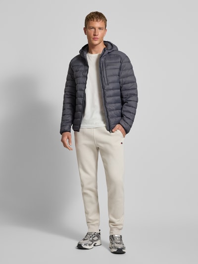Männermodel trägt Sweatpants mit elastischem Bund und Label-Stitching von CHAMPION im Regular-Fit aus Baumwoll-Mix in Beige, Ganzkörperansicht von vorne.