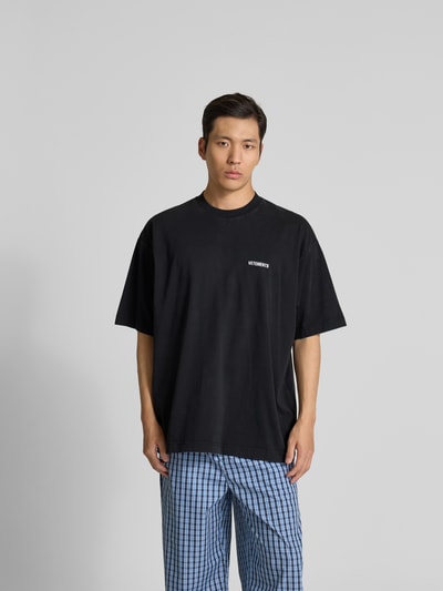 Männermodel trägt Relaxed Fit T-Shirt aus reiner Baumwolle von VETEMENTS in Schwarz mit Rundhalsausschnitt und Label-Stitching, Ganzkörperansicht von vorne.