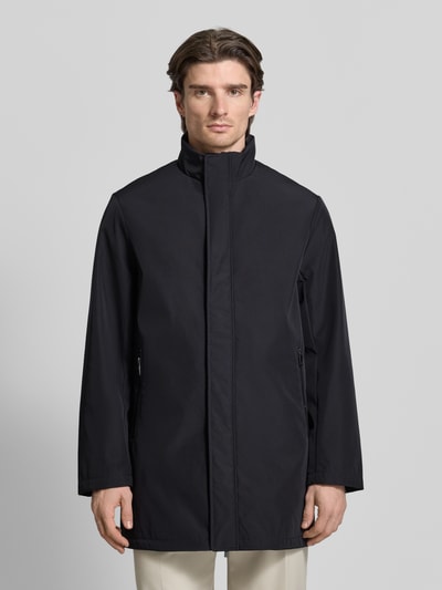 Männermodel trägt Trenchcoat mit Stehkragen von ARMANI EXCHANGE in Schwarz, gerader Schnitt, verdeckter Reißverschluss, Ganzkörperansicht von vorne.