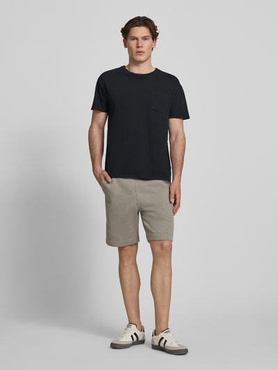 Męski model nosi T-Shirt aus Baumwoll-Leinen-Mix mit Brusttasche od Superdry, krój regular fit, okrągły dekolt, brustasza, długość tyłu w rozmiarze M: 66 cm, kolor czarny, gładka faktura, całopostaciowy widok z przodu.