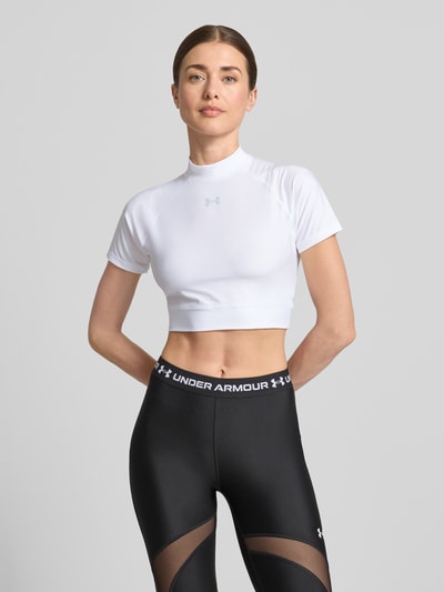 Frauenmodel trägt Cropped T-Shirt mit Logo und Stehkragen von Under Armour, weiß, Material-Mix mit Stretch-Anteil, Rückenlänge 30 cm, Ganzkörperansicht von vorne.
