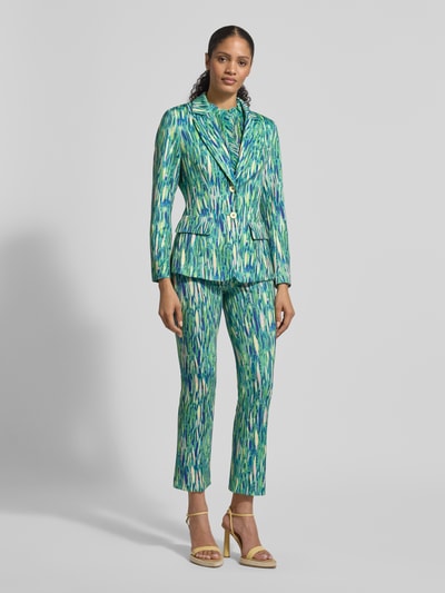 Frauenmodel trägt Slim Fit Blazer im Allover-Look von Marc Cain aus Material-Mix mit Stretch-Anteil, Reverskragen, Knopfverschluss, Pattentaschen, farbenfrohes Muster in Grün- und Blautönen, passende Hose, Ganzkörperansicht von vorne.