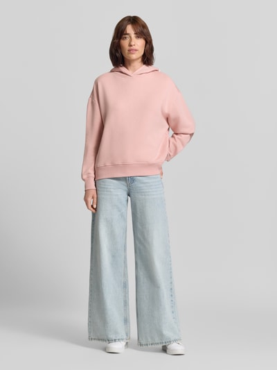Frauenmodel trägt Oversized Hoodie aus Baumwolle von Closed in Rosa mit Print und überschnittenen Schultern, locker geschnitten, Ganzkörperansicht von vorne.