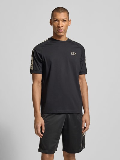 Męski model nosi T-shirt aus Viskose-Mix mit Logo od EA7 Emporio Armani, czarny, z dodatkiem streczu, krój regular fit, okrągły dekolt, logo, długość tyłu w rozmiarze M: 70 cm, widok na cały przód, proste tło.