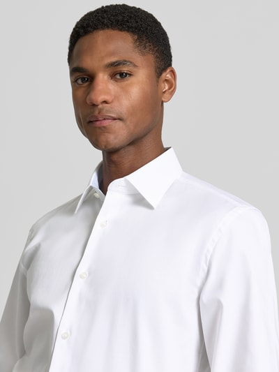 Męski model nosi Slim Fit Businesshemd aus reiner Baumwolle Modell 'HANK' von BOSS, biała popelina, długi rękaw, Kent kołnierzyk, jednorzędowa listwa guzikowa, sportowy mankiet, aplikacja z logo, wygląd jednolity, krój slim fit, widok z przodu zbliżenie na górną część ciała.