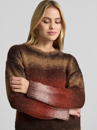 Frauenmodel trägt Strickpullover im Allover-Look mit Rundhalsausschnitt von MORE & MORE, Material-Mix mit Alpaka-Anteil, Relaxed Fit, Farbverlauf in Braun, Rot und Rosa, gerippte Textur, Nahaufnahme Oberkörper.