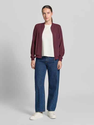 Frauenmodel trägt Regular Fit Blouson mit Reißverschluss-Detail von VERO MODA in Dunkelrot, kombiniert mit weißem Shirt und Jeans, Ganzkörperansicht von vorne.