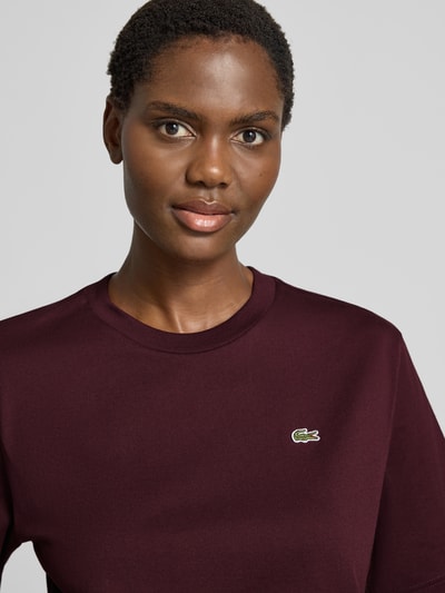 Frauenmodel trägt Relaxed Fit T-Shirt aus reiner Baumwolle von Lacoste in dunklem Bordeauxrot, Logo auf der Brust, Nahaufnahme Oberkörper. Damen T-Shirt von Lacoste.