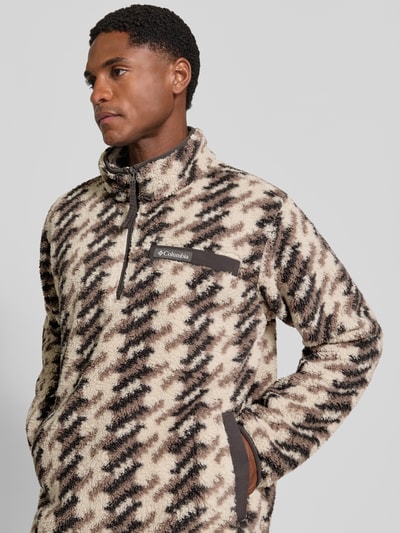 Męski model nosi Regular Fit Pullover mit Logo-Patch od Columbia, Polar, kołnierz zapinany, beżowo-czarny wzór, krój regular fit, naszywka z logo, długość tyłu w rozmiarze M: 70 cm, długość rękawów w rozmiarze M: 68 cm, zbliżenie na górną część ciała.