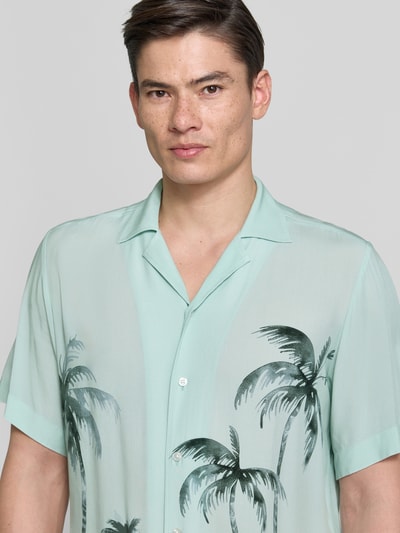 Męski model nosi Regular Fit Freizeithemd aus Viskose Modell 'RAYER_M' od BOSS Orange z nadrukiem palm, miętowy kolor, krój regular fit, resortowy kołnierzyk, krótki rękaw, czysta wiskoza, fason casual, Nahaufnahme górnej części ciała.