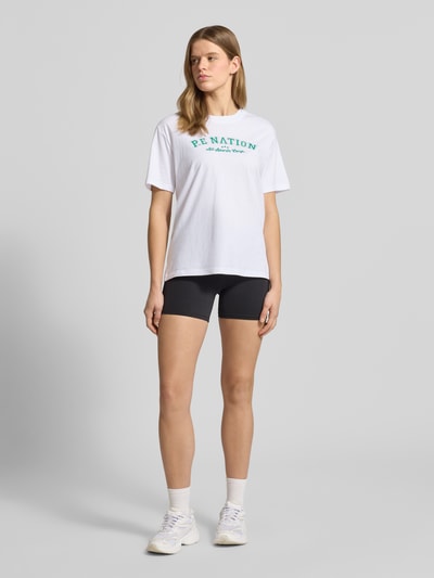 Frauenmodel trägt T-Shirt mit Logo-Print und Rundhalsausschnitt von P.E Nation aus Reine Baumwolle, Relaxed-Fit, Rückenlänge 64 cm, Ganzkörperansicht von vorne.