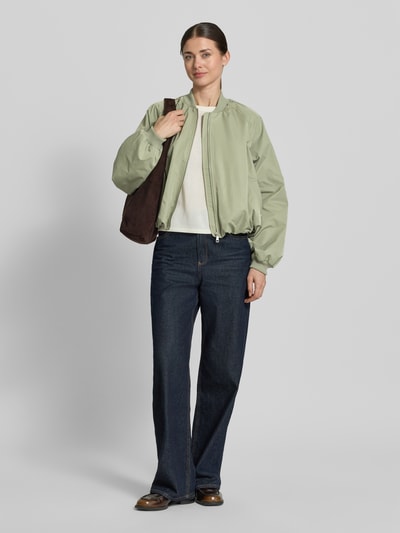 Frauenmodel trägt Blouson mit elastischen Ärmelabschlüssen und Reißverschluss von Zero in hellem Grün, kombiniert mit Loose-Fit, Stehkragen, Raglanärmel, Maße: Rückenlänge 52 cm, Schulterbreite 40 cm, Brustweite 50 cm, Ärmellänge 55 cm, Ganzkörperansicht von vorne.