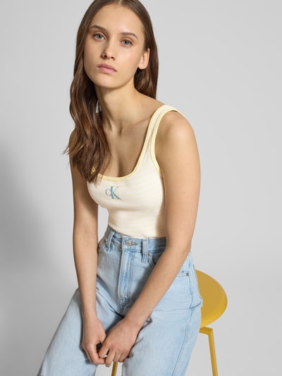 Frauenmodel trägt Trägertop in Ripp-Optik mit Logo von Calvin Klein Jeans, Slim Fit, gelb-weiß gestreift, Nahaufnahme Oberkörper.