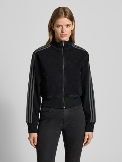 Frauenmodel trägt Jacke mit Reißverschluss von adidas Originals in Schwarz mit gerippten Abschlüssen, Stehkragen, Label-Stitching, Eingrifftaschen, Regular-Fit, Cropped, Ganzkörperansicht von vorne.