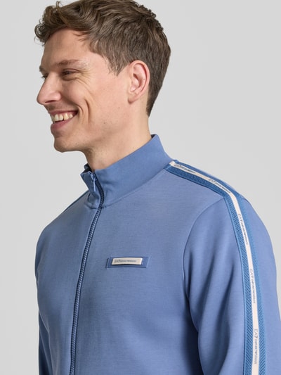 Männermodel trägt Sweatjacke aus Baumwoll-Mix von EA7 Emporio Armani in Blau mit Galonstreifen, Label-Detail, Nahaufnahme Oberkörper.