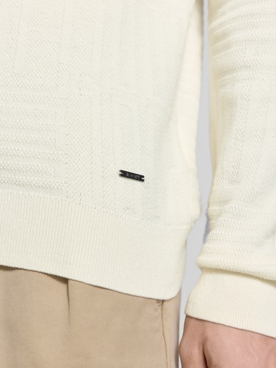 Mężczyznę model nosi Strickpullover mit gerippten Abschlüssen Modell 'Raikon' von JOOP! Collection, beżowy kolor, czysta bawełna, krój regular fit, detal przy dolnym brzegu, zdjęcie zbliżenie na dolną część tułowia.