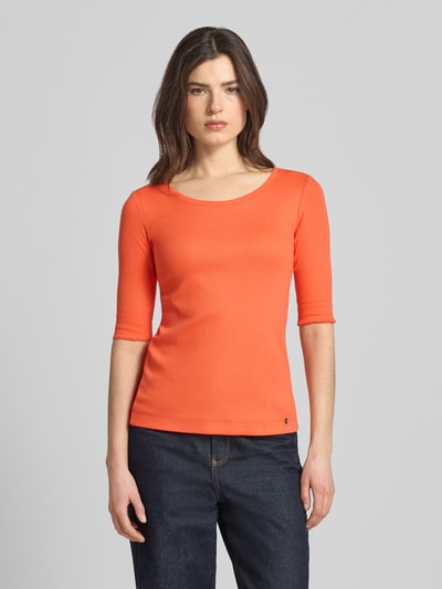 Frauenmodel trägt T-Shirt mit Label-Applikation von Marc Cain in Orange, körpernaher Schnitt, U-Ausschnitt, glatte Textur, Ganzkörperansicht von vorne.