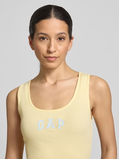 Frauenmodel trägt Slim Fit Top mit Logo-Print von GAP in Gelb, Baumwoll-Mix, Rundhalsausschnitt, Nahaufnahme Oberkörper. Rückenlänge 58 cm bei Größe S.