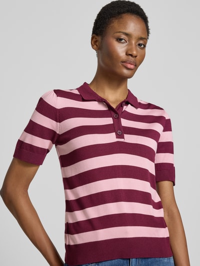 Frauenmodel trägt Regular Fit Poloshirt aus Viskose-Mix von MORE, gestreift in Pink und Bordeaux, Strick-Optik, Nahaufnahme Oberkörper.