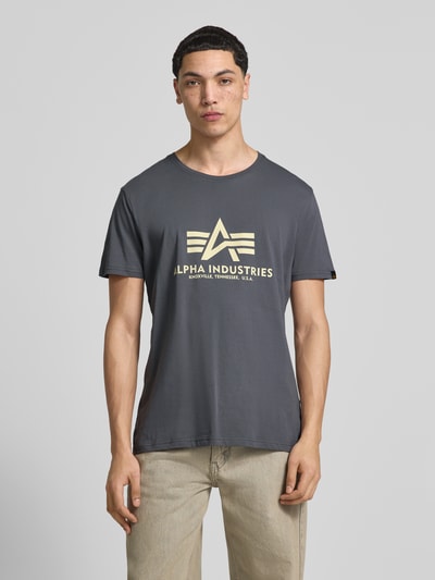 Männermodel trägt T-shirt mit labeldetail model 'BASIC' van Alpha Industries in grijs, puur katoen, recht model, ronde hals, ruglengte maat M 69 cm, ganzkörperansicht van voren.