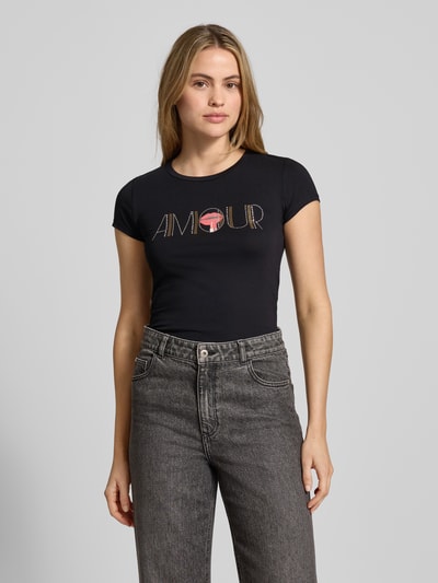 Vrouwenmodel draagt T-shirt met Ziersteinbesatz van Guess, zwart, mix van katoen en elastaan, slim fit, ronde hals, ruglengte maat S 65 cm. Nahaufnahme Oberkörper.