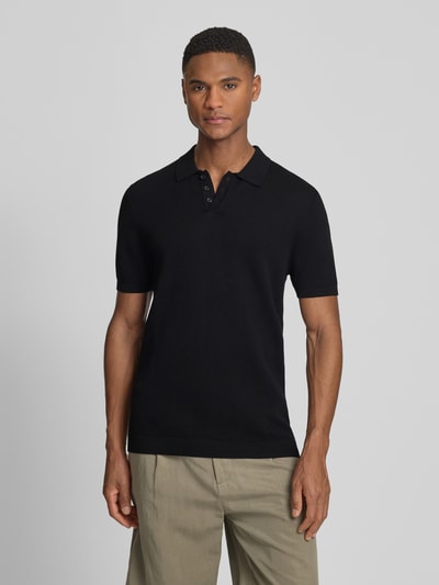Männermodel trägt schwarzes Slim-Fit Poloshirt Modell 'Triton' von Drykorn aus Reine Baumwolle mit Polokragen und Strukturmuster, Kurzärmelig, Rückenlänge bei Größe M 67 cm, Ganzkörperansicht von vorne.