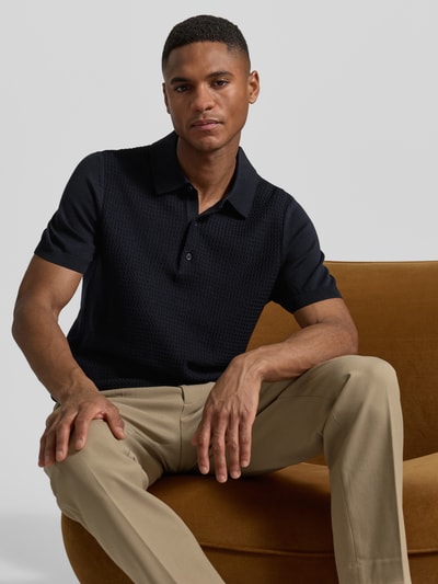 Męski model nosi Regular Fit Poloshirt aus reiner Baumwolle von Strellson, czarny, imitacja dzianiny, fakturowany wzór, drobny splot, kołnierzyk polo, dekolt w serek, krótkie rękawy z prążkowanym wykończeniem, wykończenie z prążkowanej dzianiny, 100% bawełna, krótka listwa guzikowa, widok na górną część ciała z przodu.