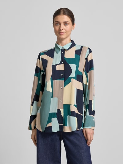 Frauenmodel trägt Relaxed Fit Hemdbluse aus reiner Viskose von Tom Tailor mit Allover-Muster in Blau, Beige und Grün, einreihige Knopfleiste, langarm, Manschette, Hemdblusenkragen, Seitenschlitzen und Schleifen-Details, Ganzkörperansicht von vorne.