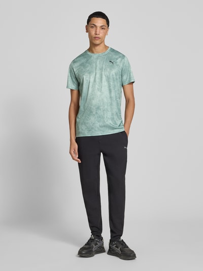 Männermodel trägt Regular Fit Sport-T-Shirt mit Logo-Print Modell 'M TAD ESSENTIALS' von PUMA in Mintgrün, schwarze Hose, Ganzkörperansicht von vorne, Herren Sport-T-Shirt von PUMA Performance.