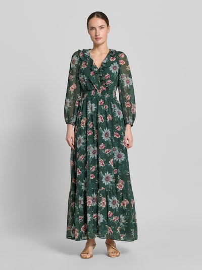 Frauenmodel trägt Maxikleid mit Volantsaum und V-Ausschnitt von Zero in dunklem Grün mit floralem Muster, taillierter Schnitt, Rüschen, Smok-Detail, elastische Ärmelabschlüsse, blickdichtes Unterkleid, Rückenlänge 140 cm bei Größe 36, Ganzkörperansicht von vorne.