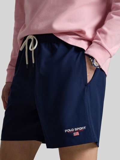 Mannelijk model draagt 'Badeshorts mit Label Stitching' van Polo Ralph Lauren in effen donkerblauw met label stitching, elastische tailleband, tunnelkoord, zijzakken en achterzak, close-up van de heupen.